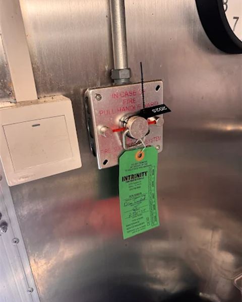 Kitchen fire suppression pull station with a green Intrinity inspection tag