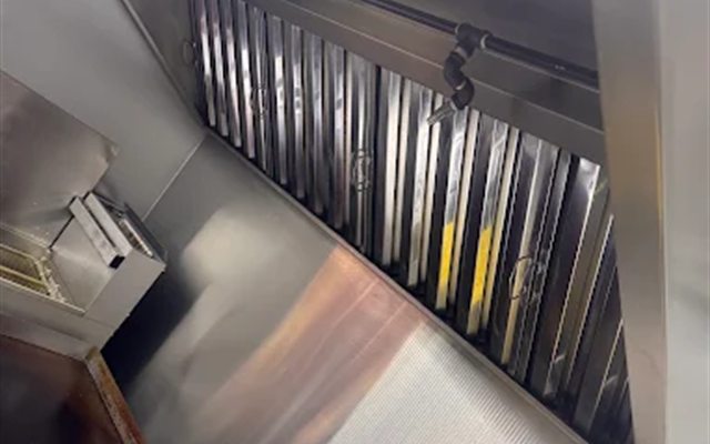 Stainless commercial kitchen hood with grease filters over a cooking line